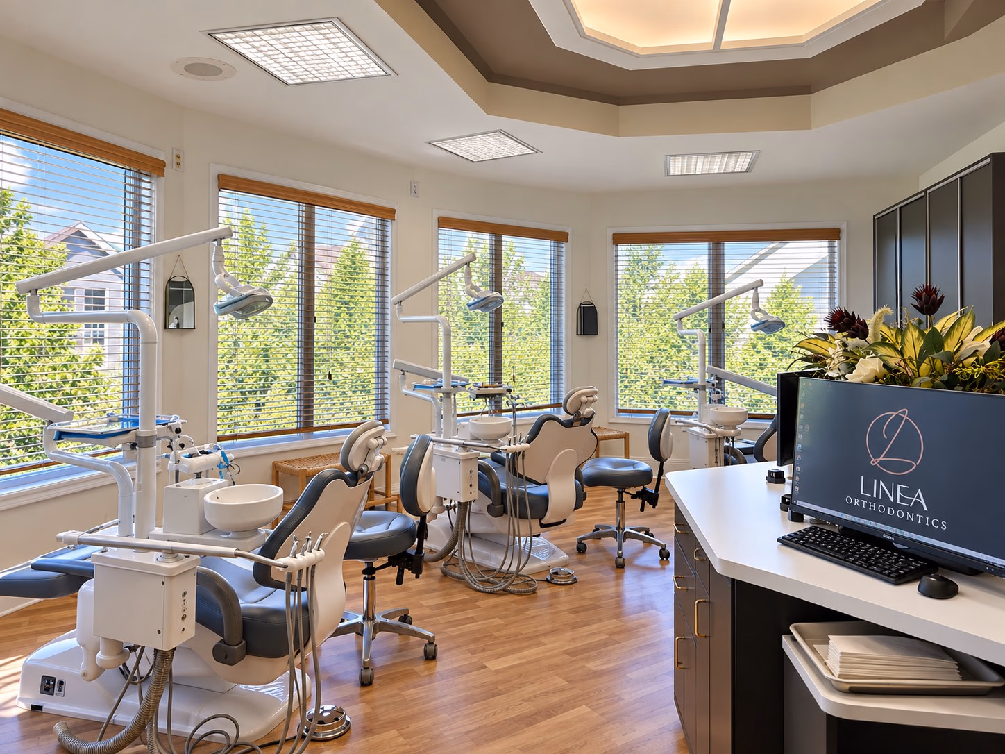 Open treatment area with orthodontic chairs beneath a wall of windows
